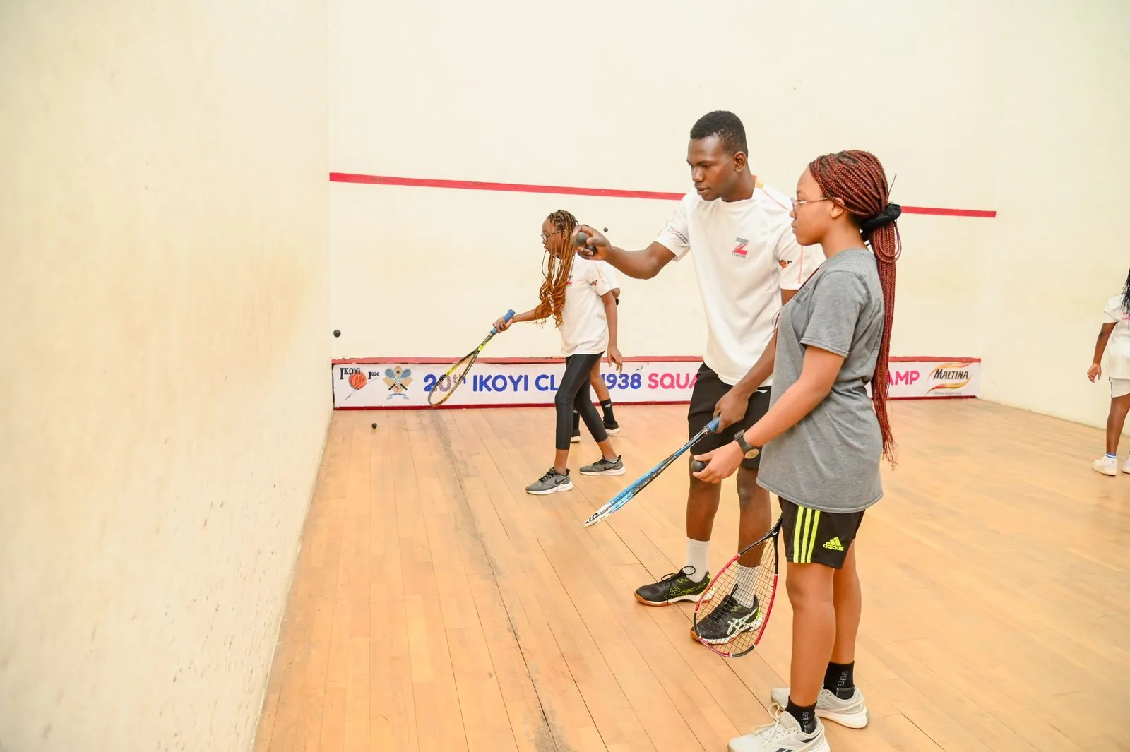 A coach guiding a young girl through a squash drill