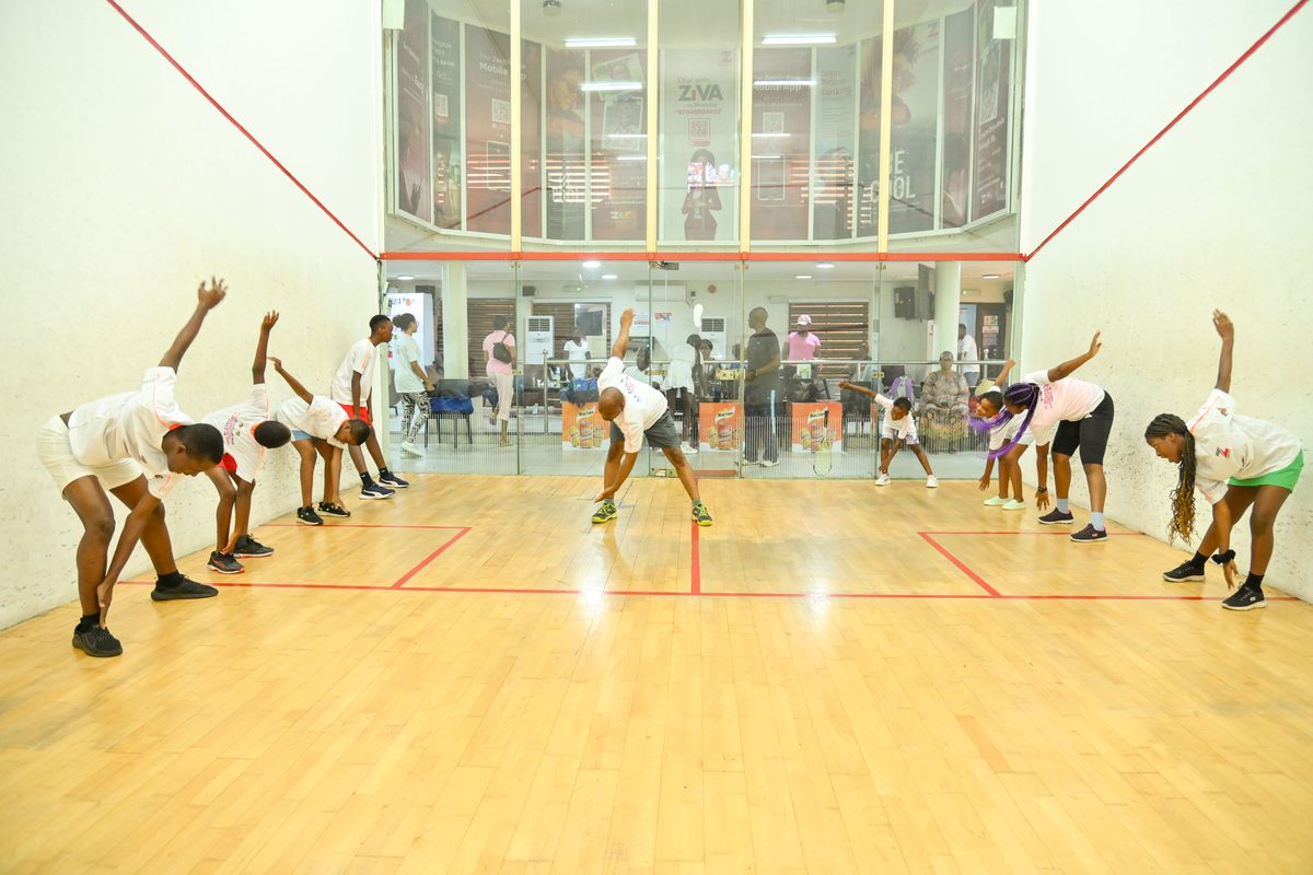 Coach leading a group warm-up on court, young participants mirroring his stretching stance at the Ikoyi Club Squashtival Summer Camp