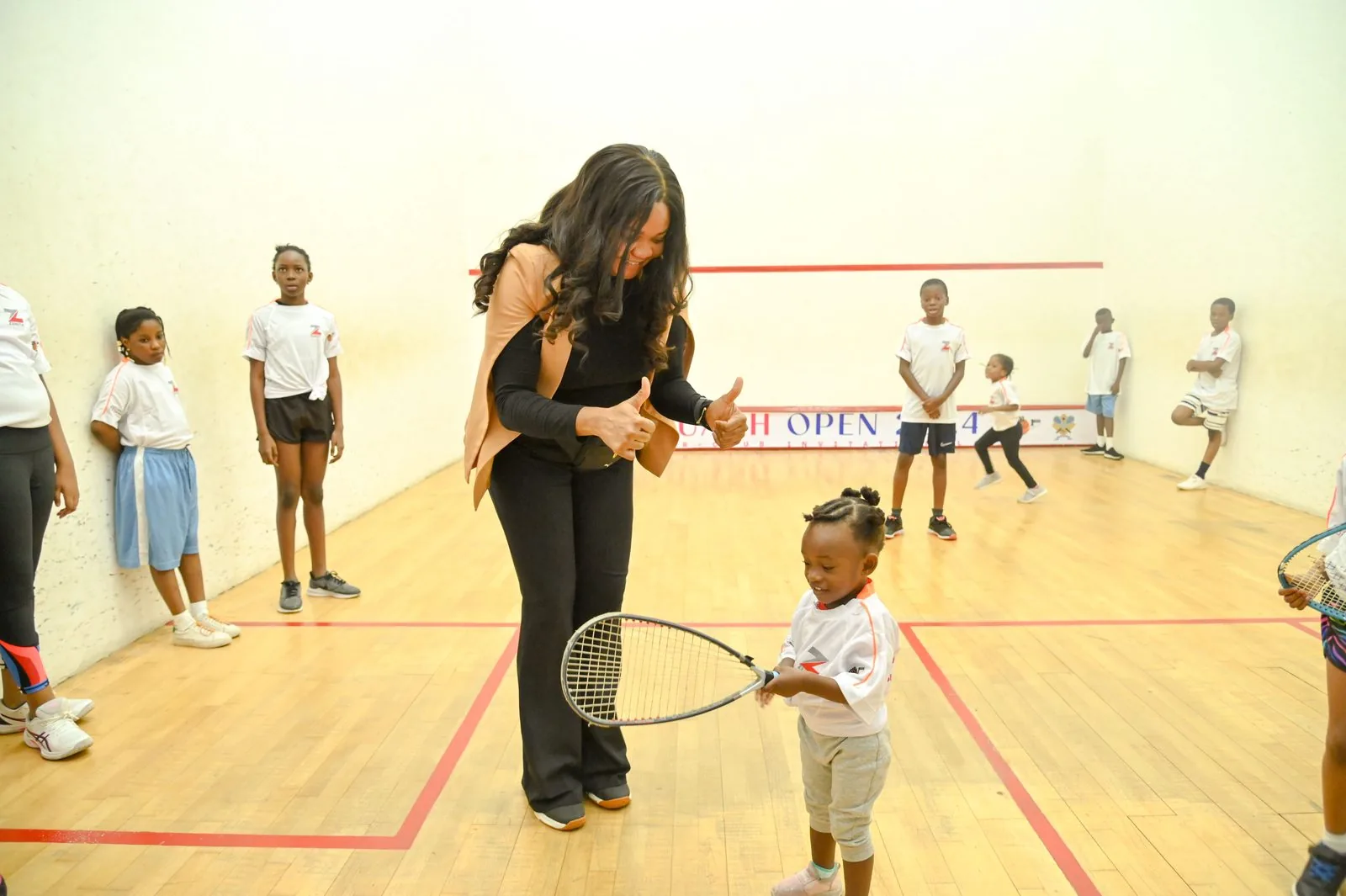 A coach giving a thumbs up to a young child holding a racket